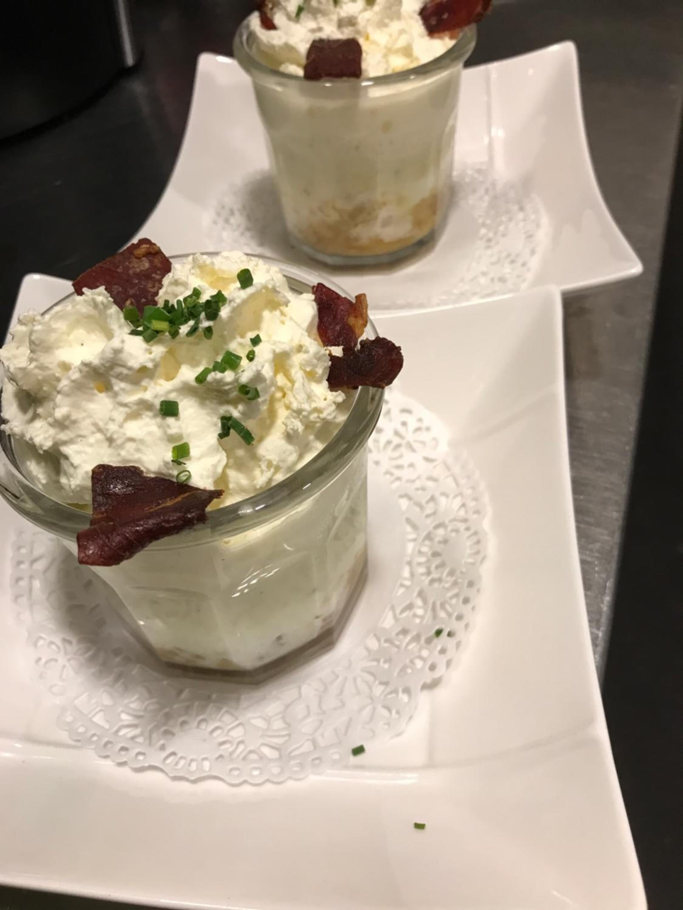 Duas taças de sobremesa com chantilly e guarnição de bacon sobre um prato branco.