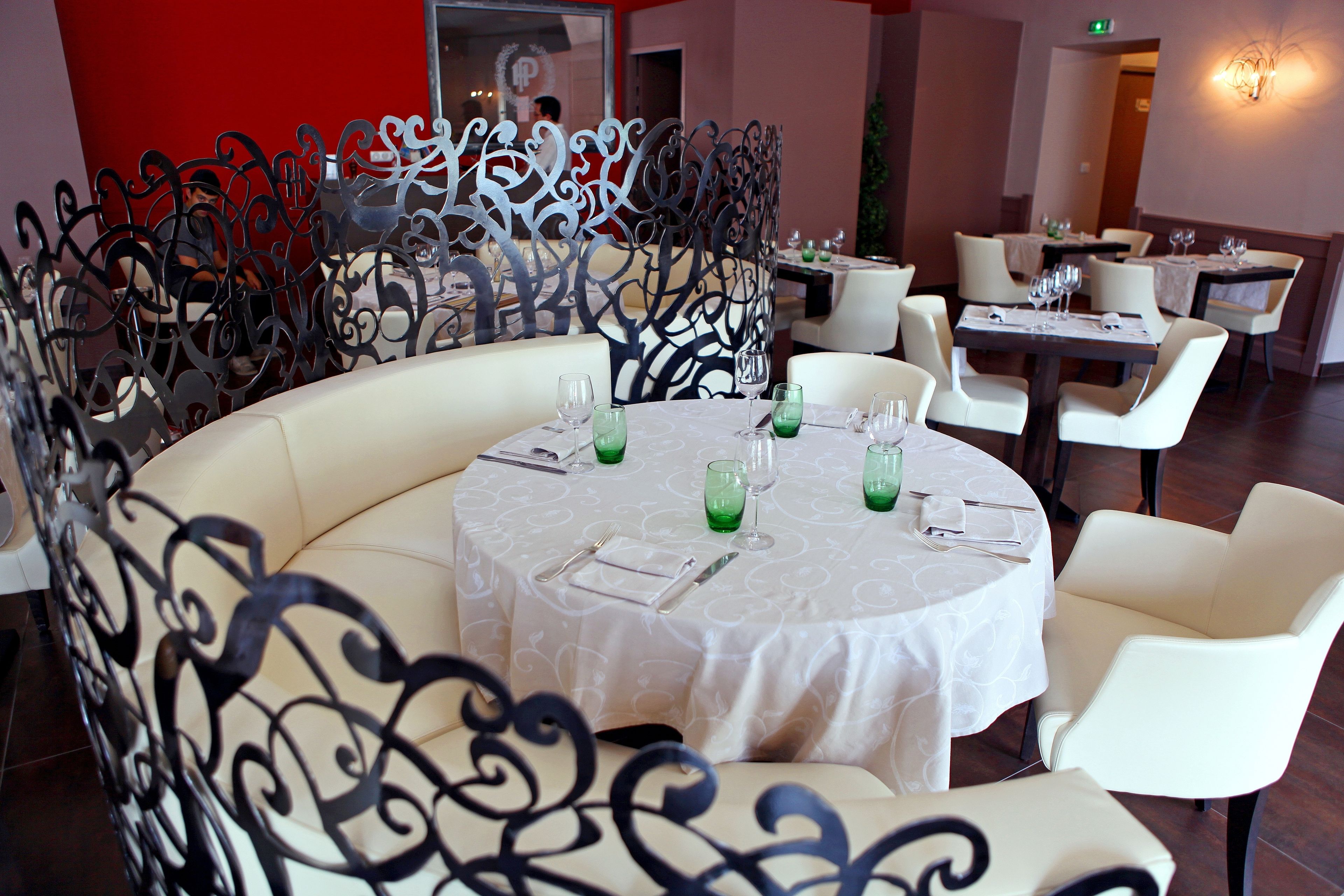 A restaurant with round tables, white chairs, and a decorative metal partition.