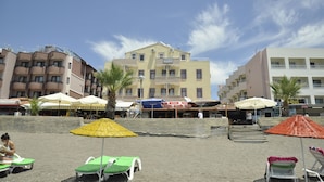 Un hotel frente a la playa con varios balcones, mobiliario exterior y sombrillas.
