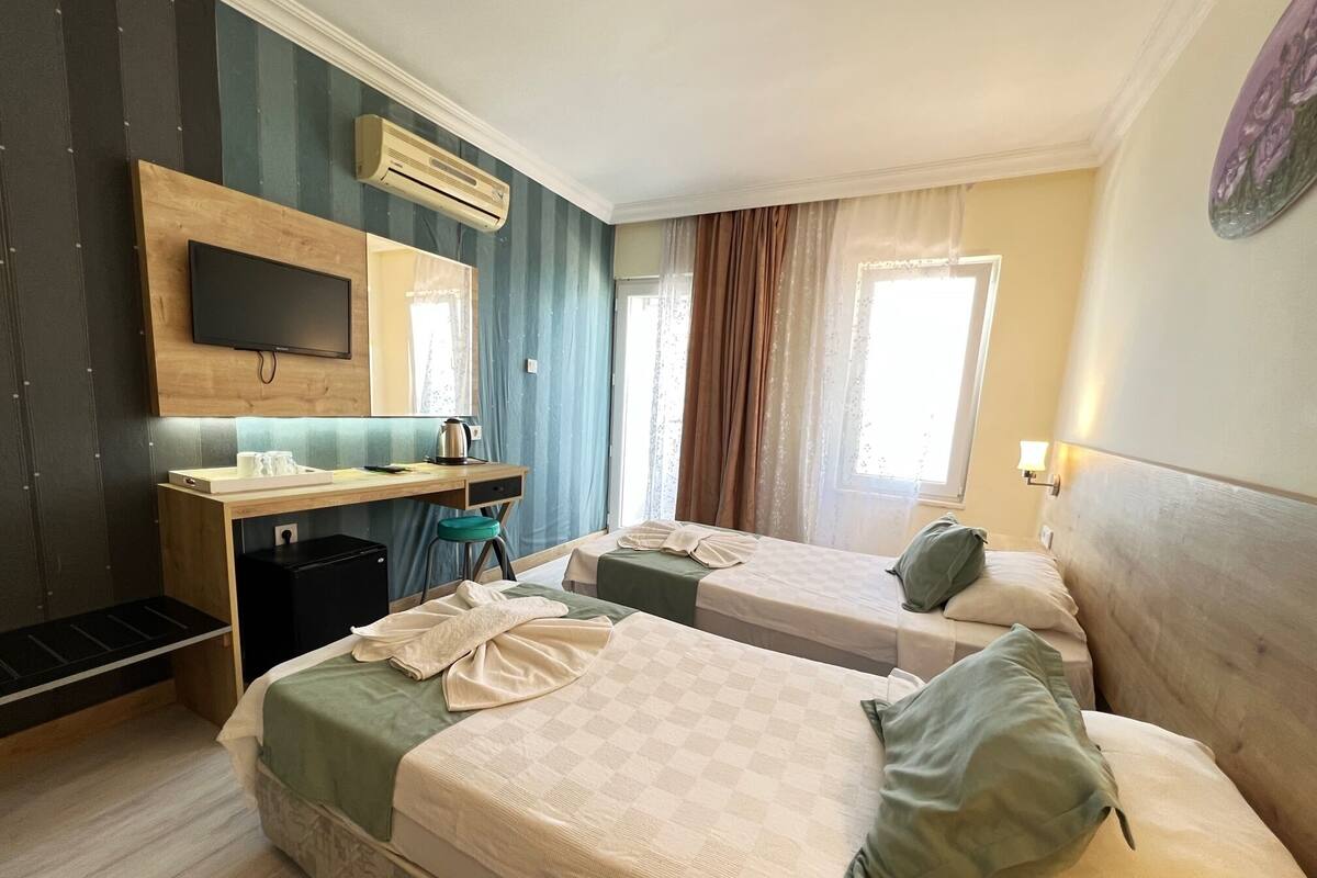Une chambre d’hôtel avec deux lits, un bureau avec une chaise, une télévision et une fenêtre avec des rideaux.