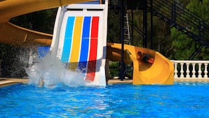 Un tobogán de agua con llamativas rayas verticales de colores, una piscina y una estructura de madera.