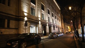 Vista nocturna de una calle con coches aparcados y un edificio con ventanas iluminadas.
