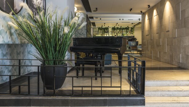 Un vestíbulo con un piano de cola, una planta grande en maceta y un mostrador de recepción.