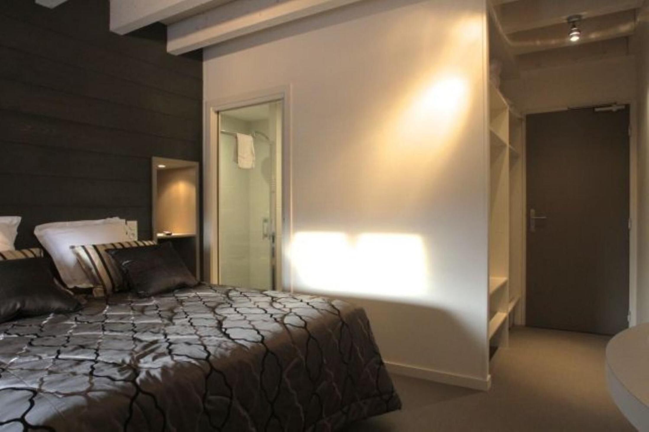 A modern hotel room with a large bed, a walk-in closet, and a bathroom.