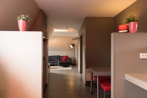 Ein modernes Hotelzimmer mit Küchenzeile, Essecke und Wohnbereich mit einer Couch und roten Kissen.