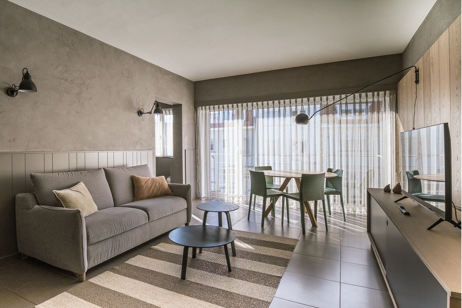 Un salon moderne avec un canapé gris, une petite table ronde et un coin repas avec des chaises.