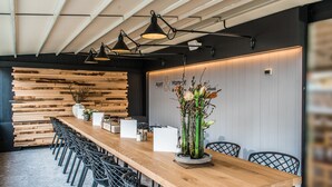 Ein langer Holztisch mit schwarzen Stühlen, eine Blumenvase und eine Wand mit Holzlatten und einem Schild.