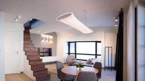 Ein modernes Interieur mit einer Treppe zu einer Küche, einem Essbereich mit rundem Tisch und einem großen Fenster, das natürliches Licht hereinlässt.