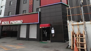 A multi-story building with a prominent vertical stripe pattern on the facade, a red and white sign indicating a motel parking area, and a visible entrance with a door. - V Hotel (Busan)
