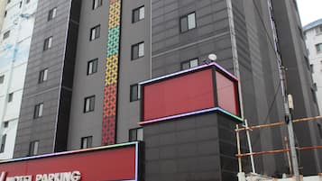 A multi-story building with a prominent vertical stripe pattern on the facade, a red and white sign indicating a motel parking area, and a visible entrance with a door.