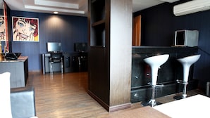 A modern hotel lobby with a wooden floor, a bar area with stools, a television, and a painting on the wall. - V Hotel (Busan)