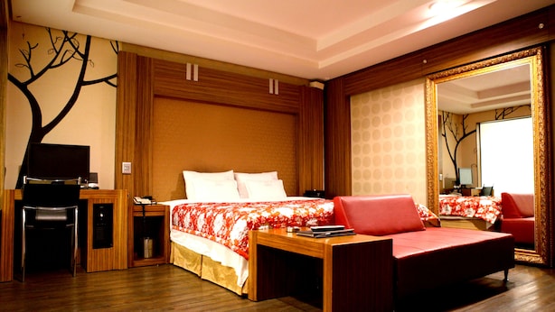 A hotel room with a wooden desk, a bed with a red and white floral bedspread, a red sofa, and a large mirror with a gold frame. - V Hotel (Busan)