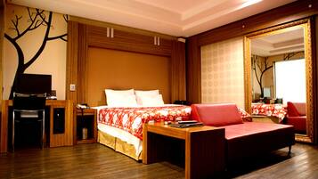 A hotel room with a wooden desk, a bed with a red and white floral bedspread, a red sofa, and a large mirror with a gold frame.