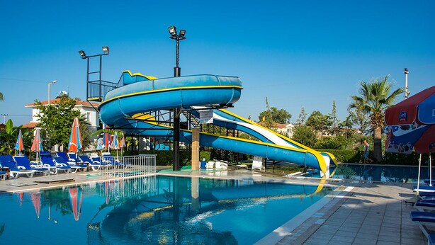 A swimming pool with a water slide, lounge chairs, and umbrellas. - Hotel Nazar Garden (Fethiye)