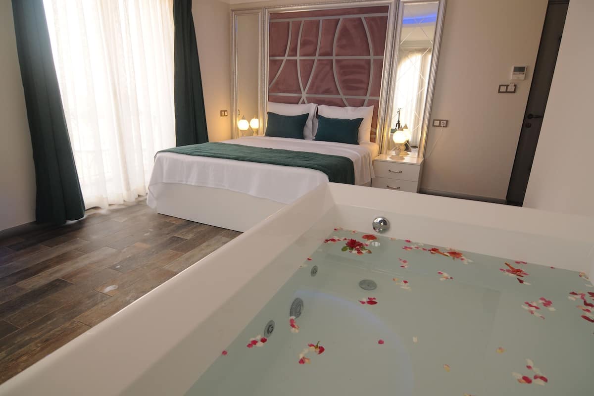 Une chambre d’hôtel avec une grande baignoire, un lit avec une literie verte et un miroir au-dessus du lit.