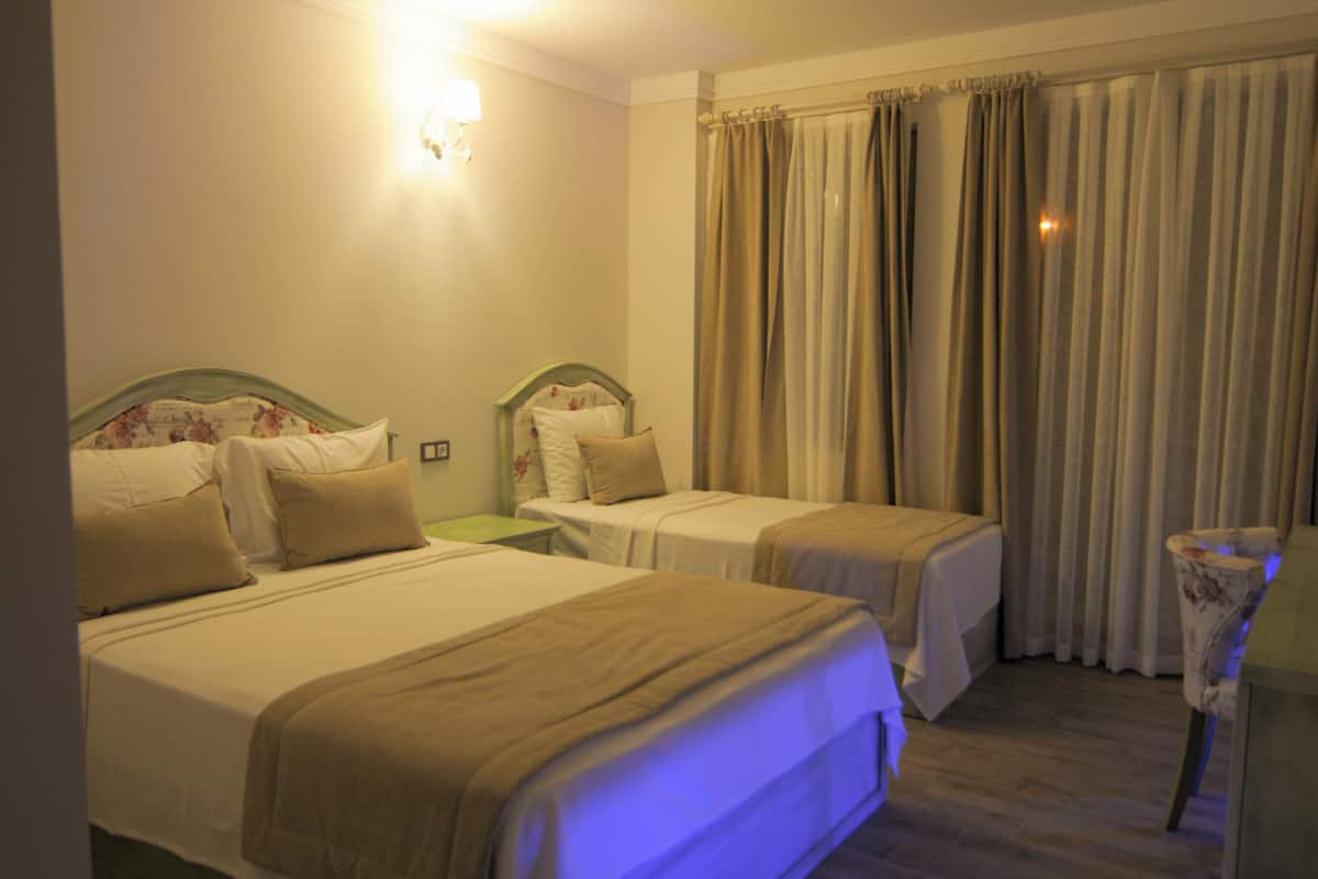 Une chambre d’hôtel avec deux lits simples, une table de chevet, une lampe et un rideau.