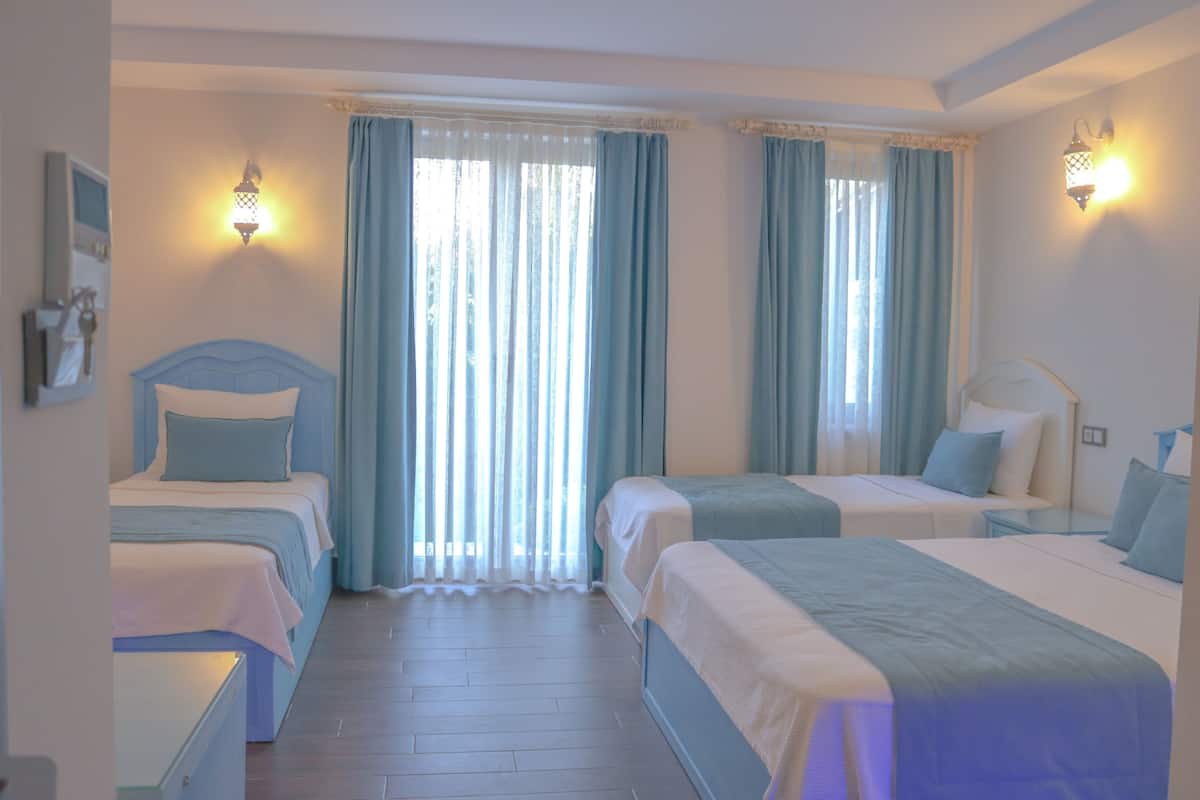 Une chambre d’hôtel avec deux lits, une grande fenêtre avec des rideaux et des lampes fixées au mur.