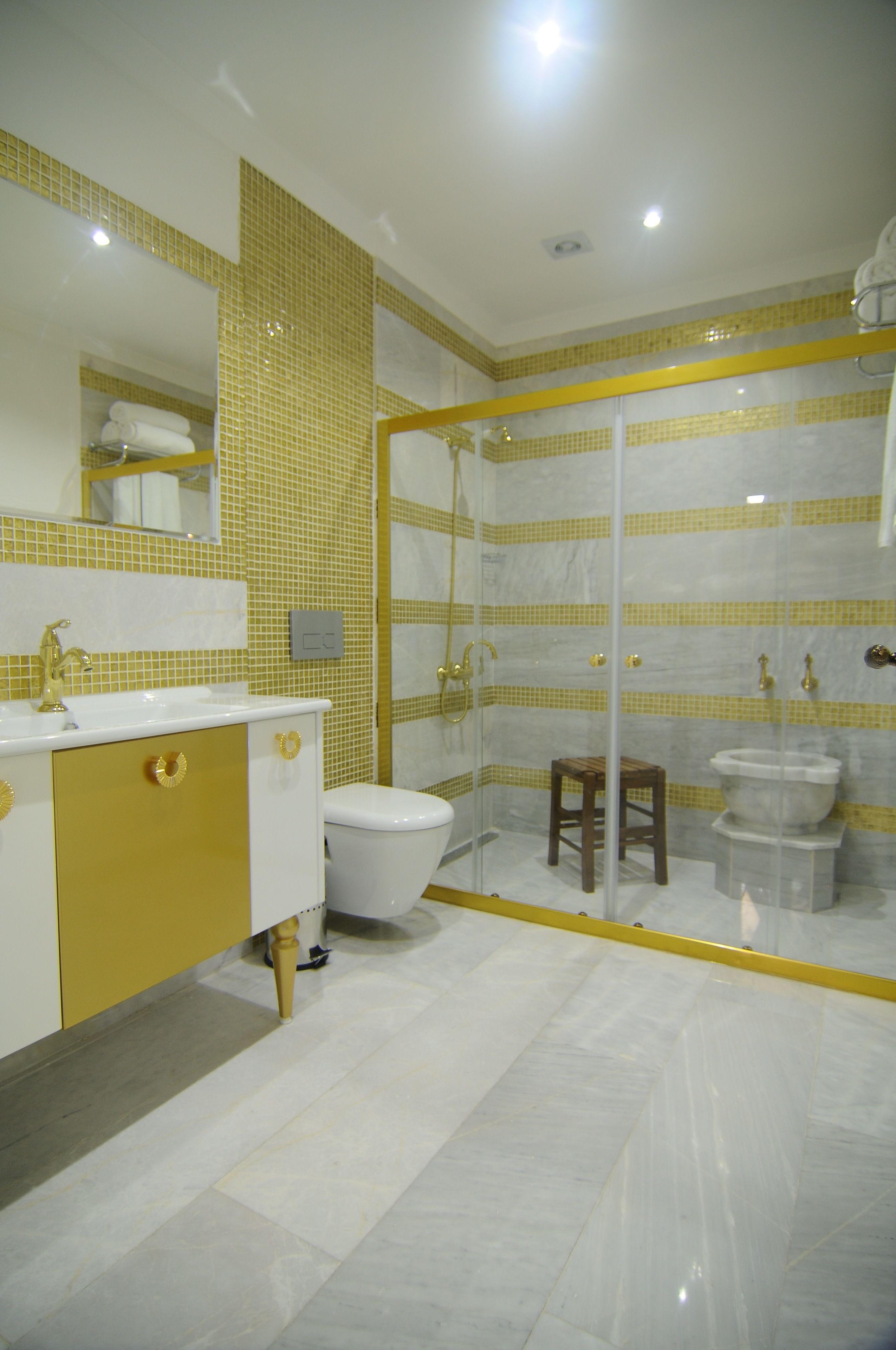 A bathroom with a white sink, gold cabinet, and yellow-tiled walls.