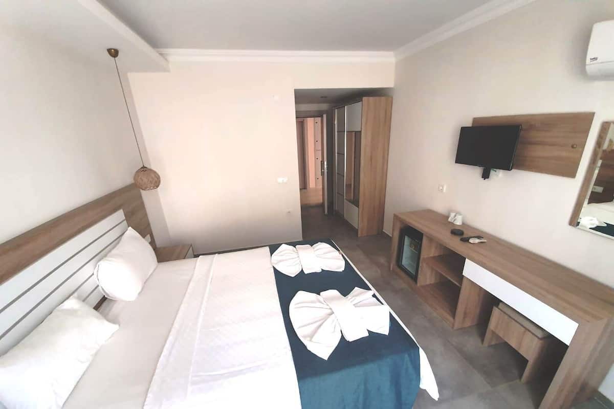 A hotel room with a bed, bedside table, TV, and a desk with a chair.