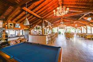 Una mesa de billar en una sala con suelo de madera, zona de recepción y bar.