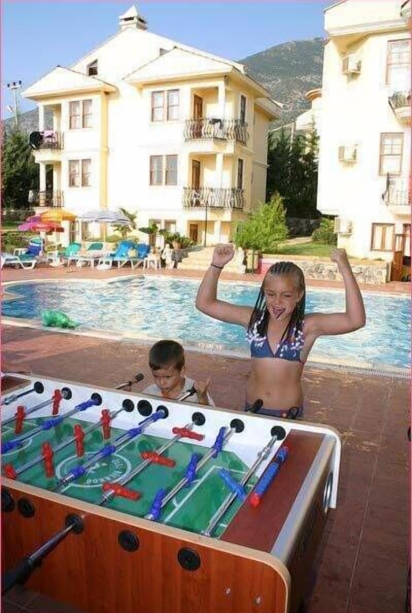 A poolside area with a foosball table, lounge chairs, and a building with balconies.