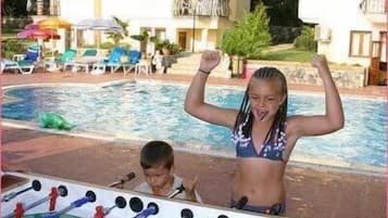 A poolside area with a foosball table, lounge chairs, and a building with balconies.