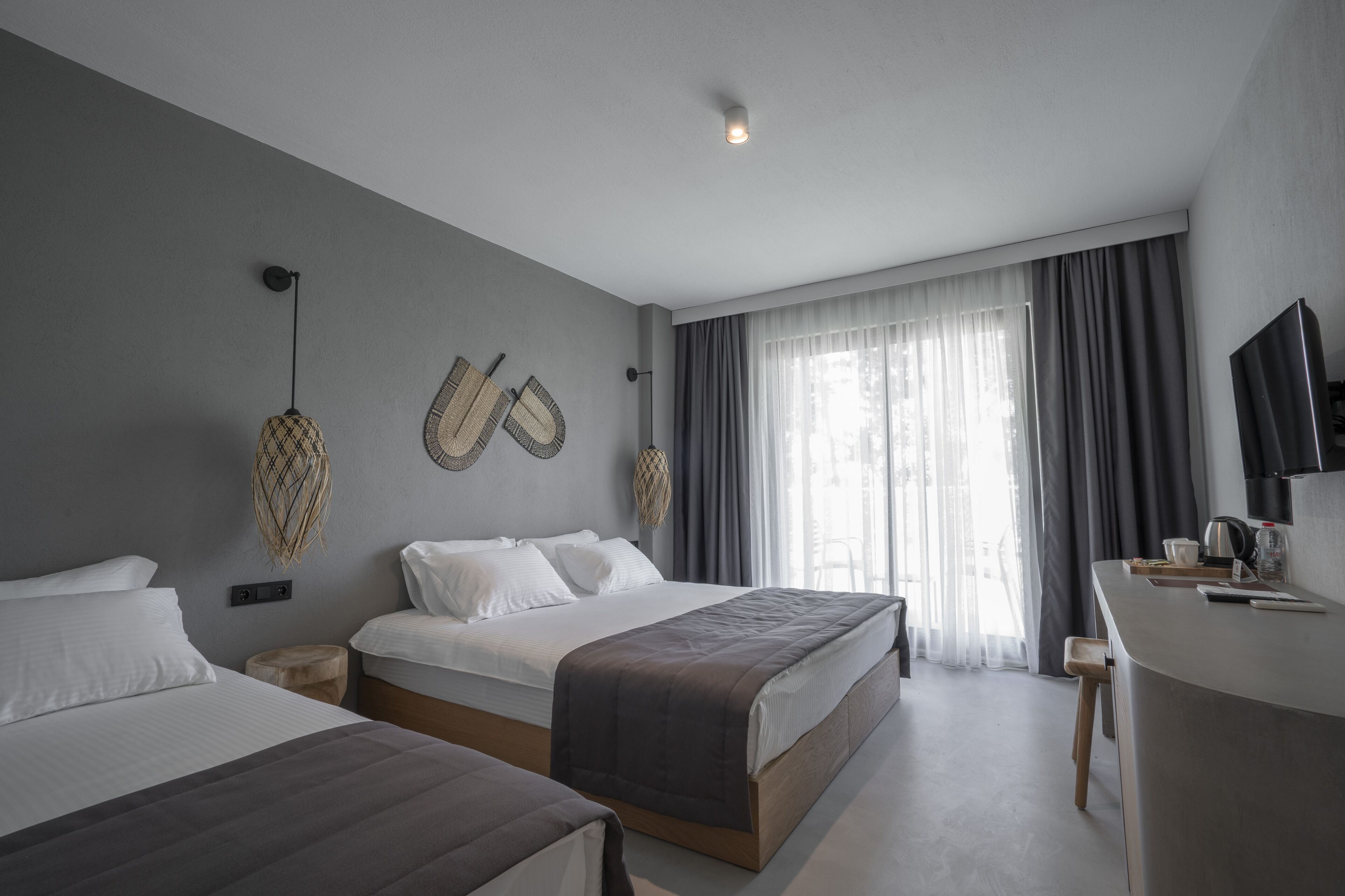 Quarto de hotel moderno com duas camas, uma mesa de trabalho e uma janela grande com cortinas.