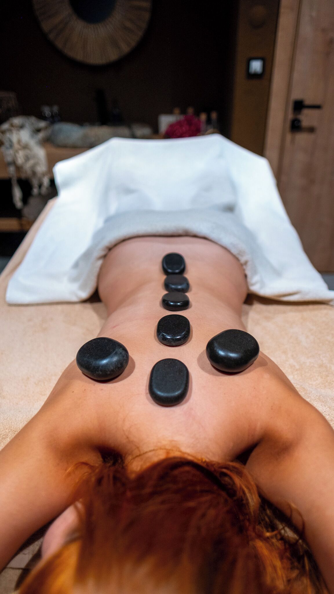 Une personne allongée sur le ventre, avec des pierres placées sur le dos, probablement dans le cadre d’un massage ou d’une séance de thérapie.
