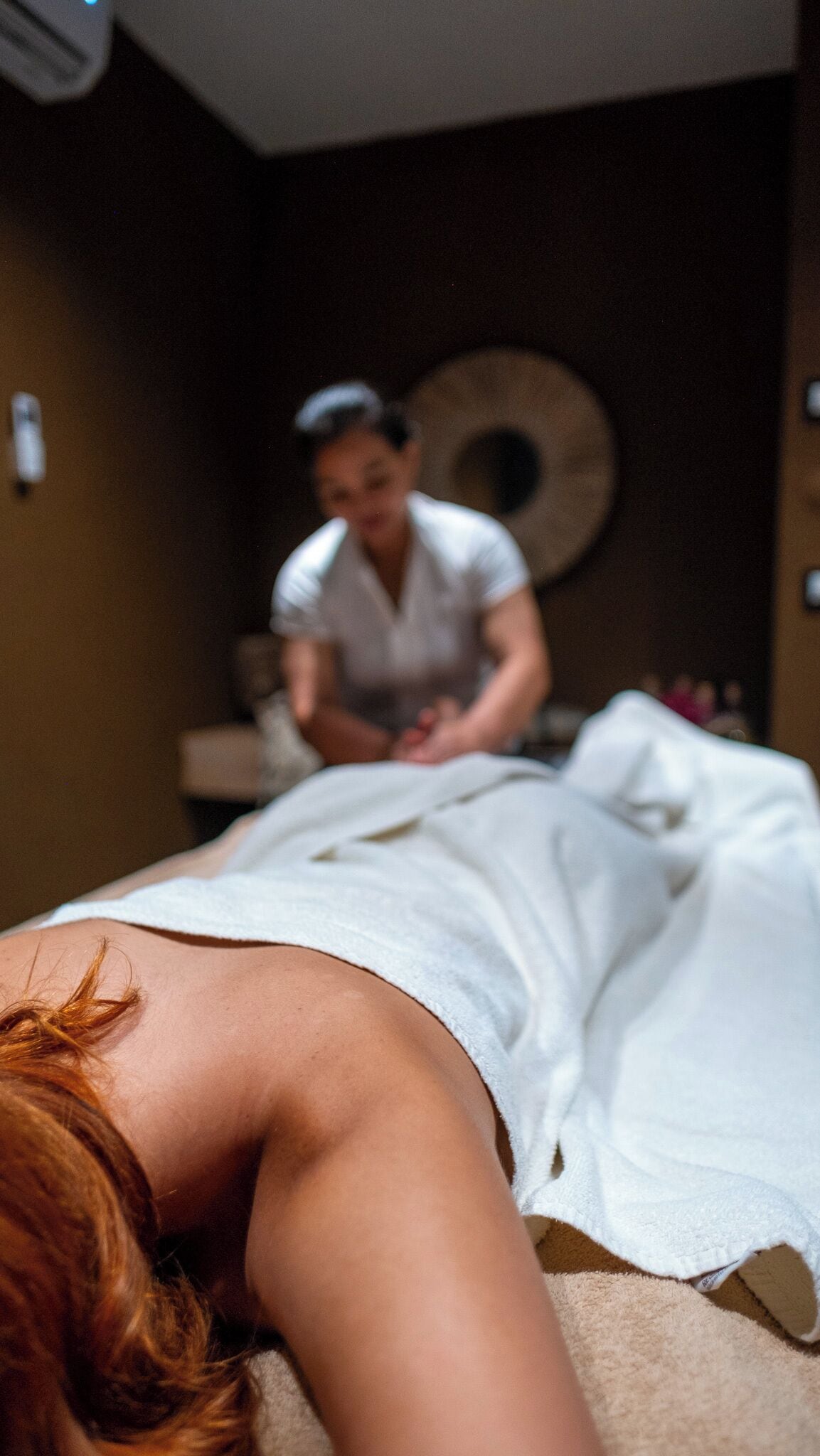 A person lying on a massage table in a room with a large circular wall decoration.