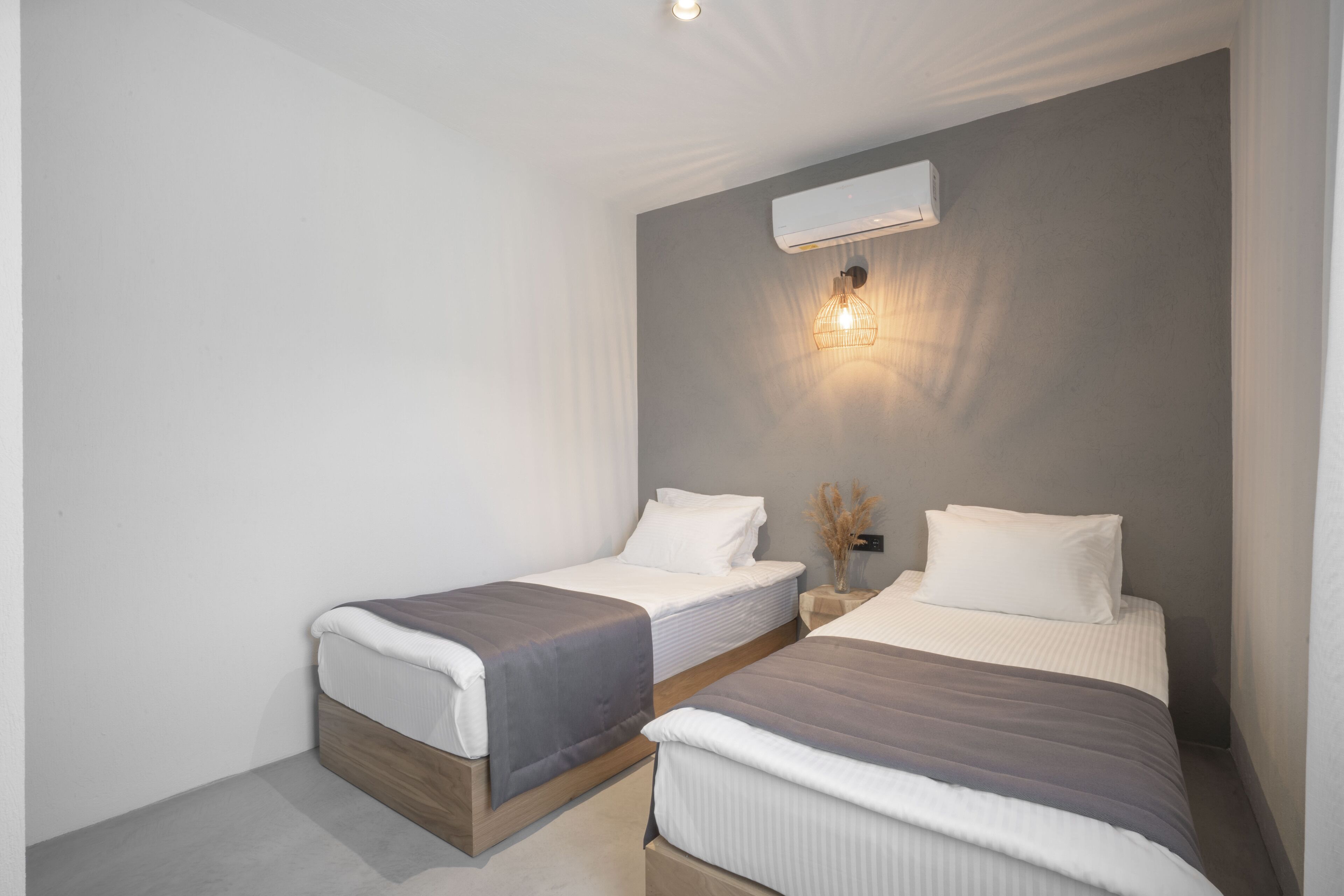 A modern bedroom with two beds, a wall-mounted air conditioner, and a bedside lamp.