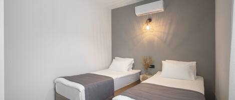 A modern bedroom with two beds, a wall-mounted air conditioner, and a bedside lamp.
