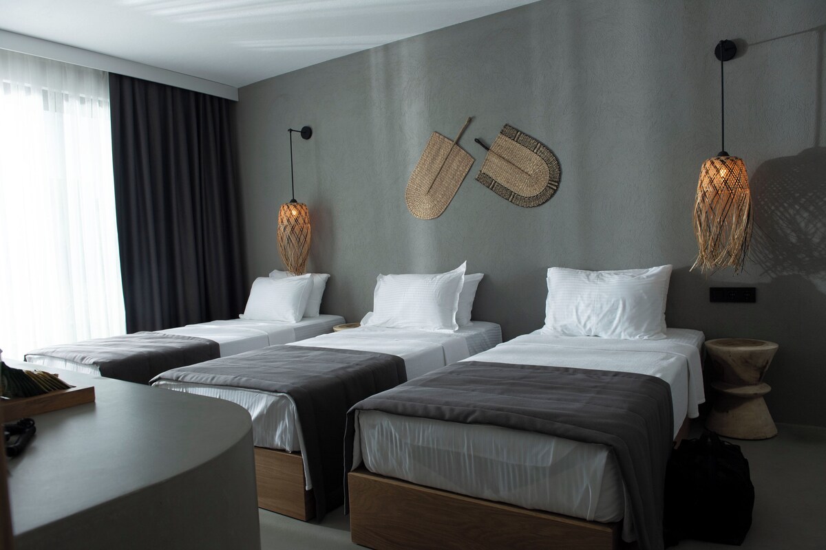 A hotel room with three beds, a round table, and a large window with curtains.