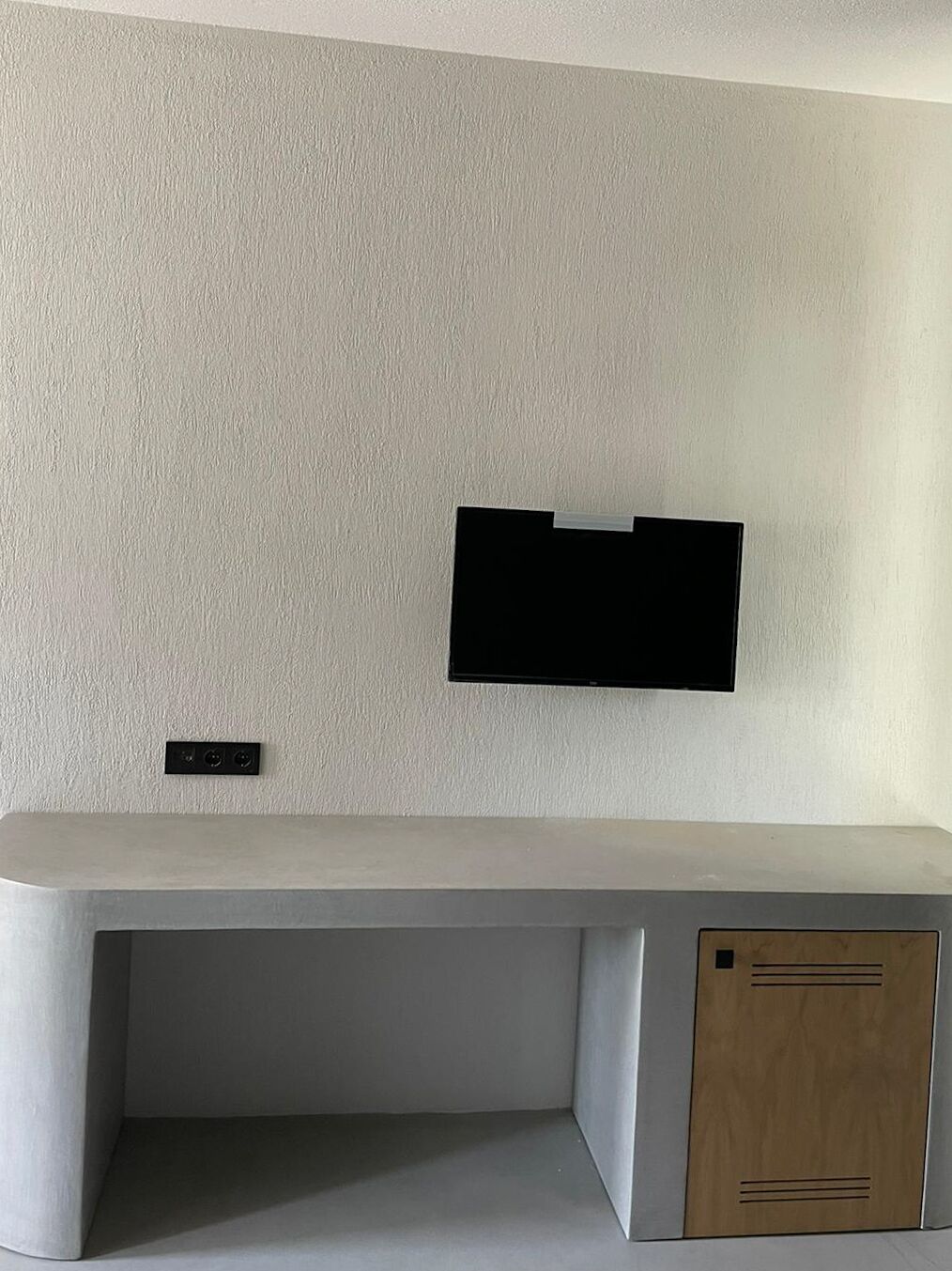 Une chambre moderne et minimaliste, dotée d’un bureau intégré et d’un téléviseur à écran plat fixé au mur.