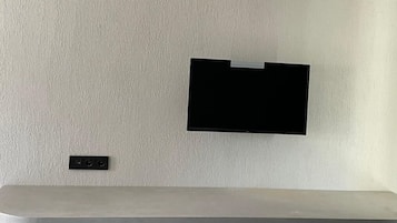 Une chambre moderne et minimaliste, dotée d’un bureau intégré et d’un téléviseur à écran plat fixé au mur.