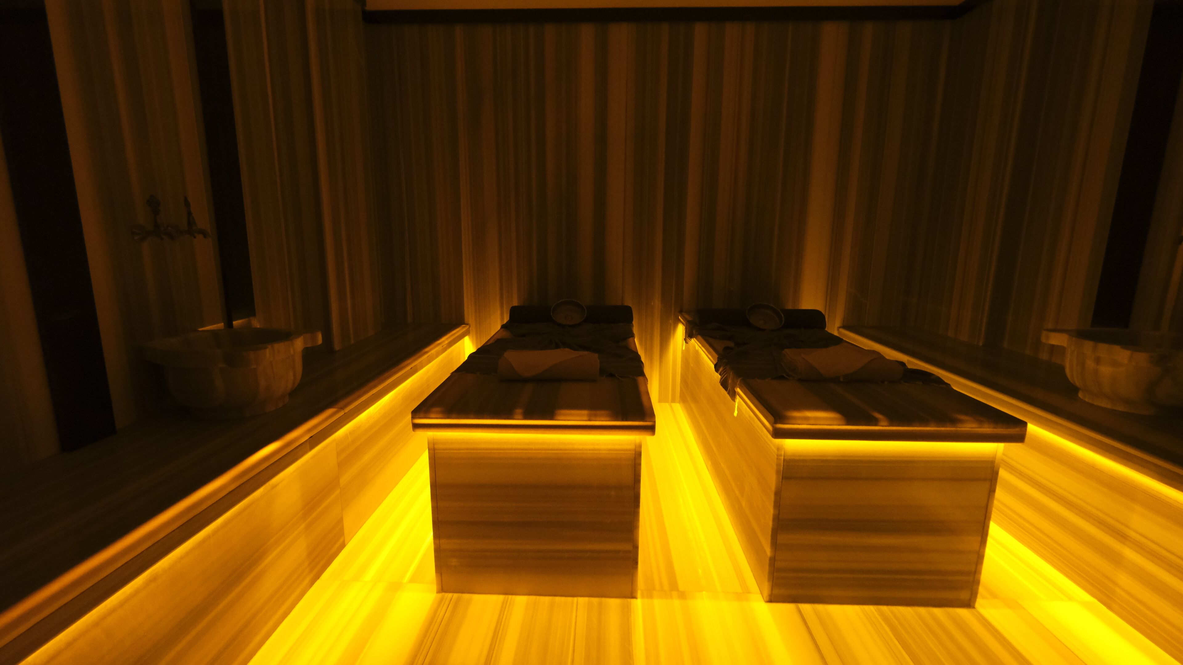 A room with two beds, wooden flooring, and a warm yellow lighting.