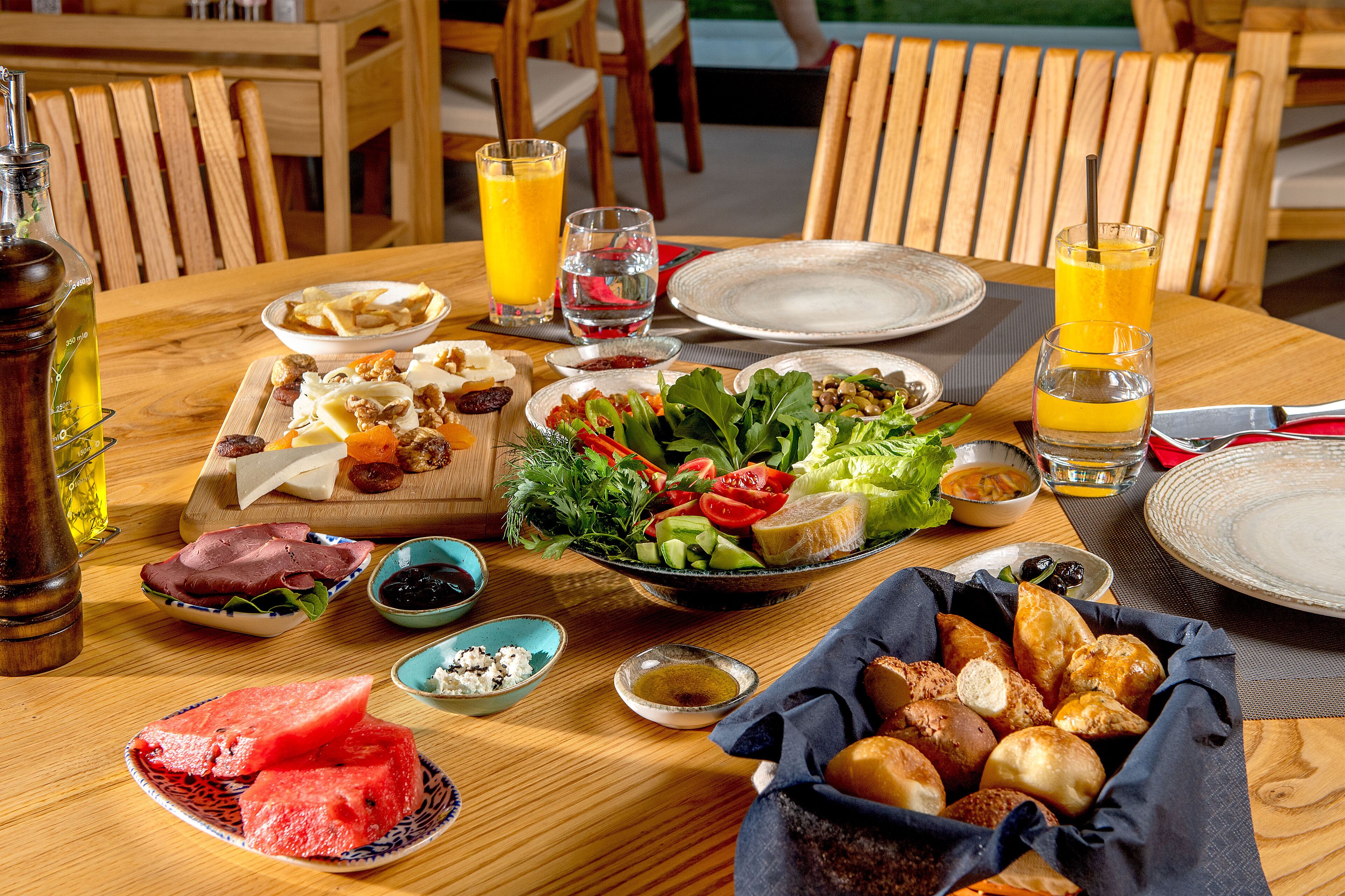 A wooden dining table with a variety of foods including a salad, meats, and bread, along with glasses of orange juice and water.