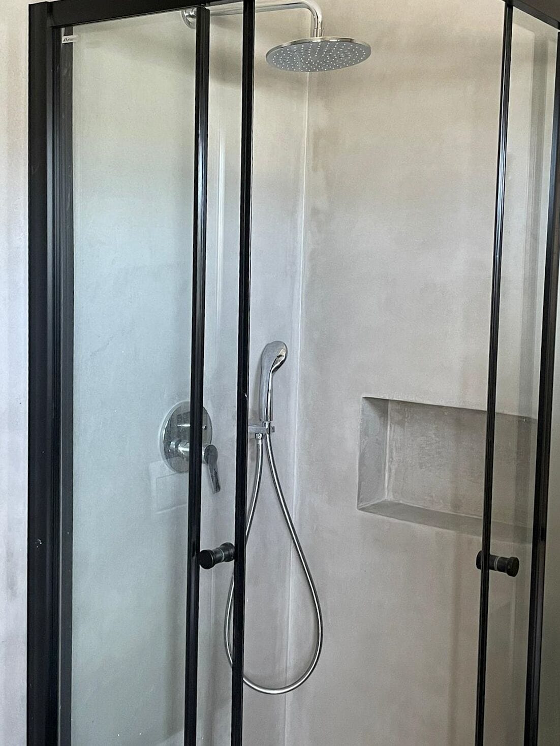 A glass-enclosed shower with a handheld showerhead and a wall-mounted control panel.