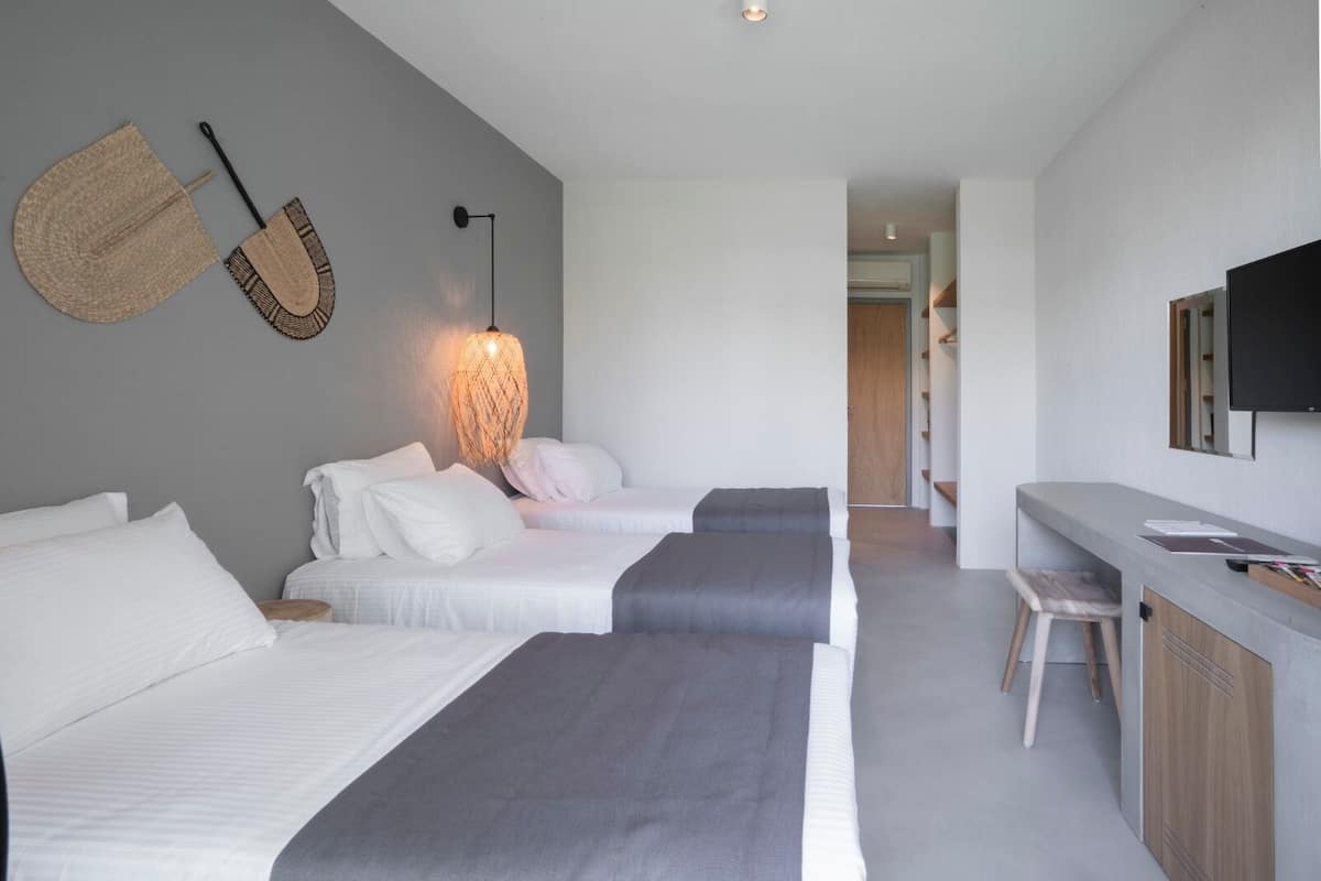 A modern hotel room with three beds, a desk, and a television.