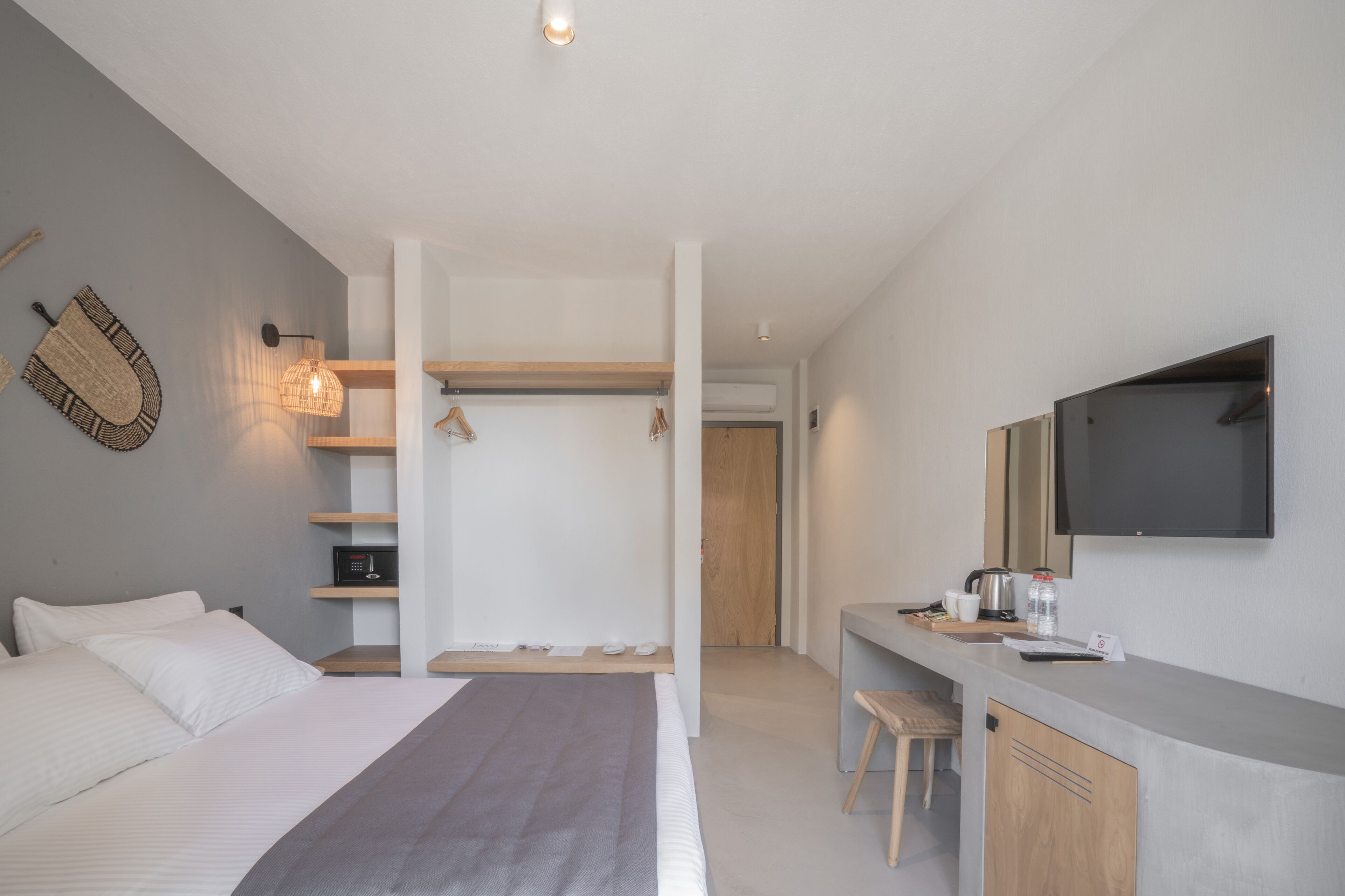 Een moderne hotelkamer met een bed, nachtkastje, bureau met stoel, televisie en garderobe.