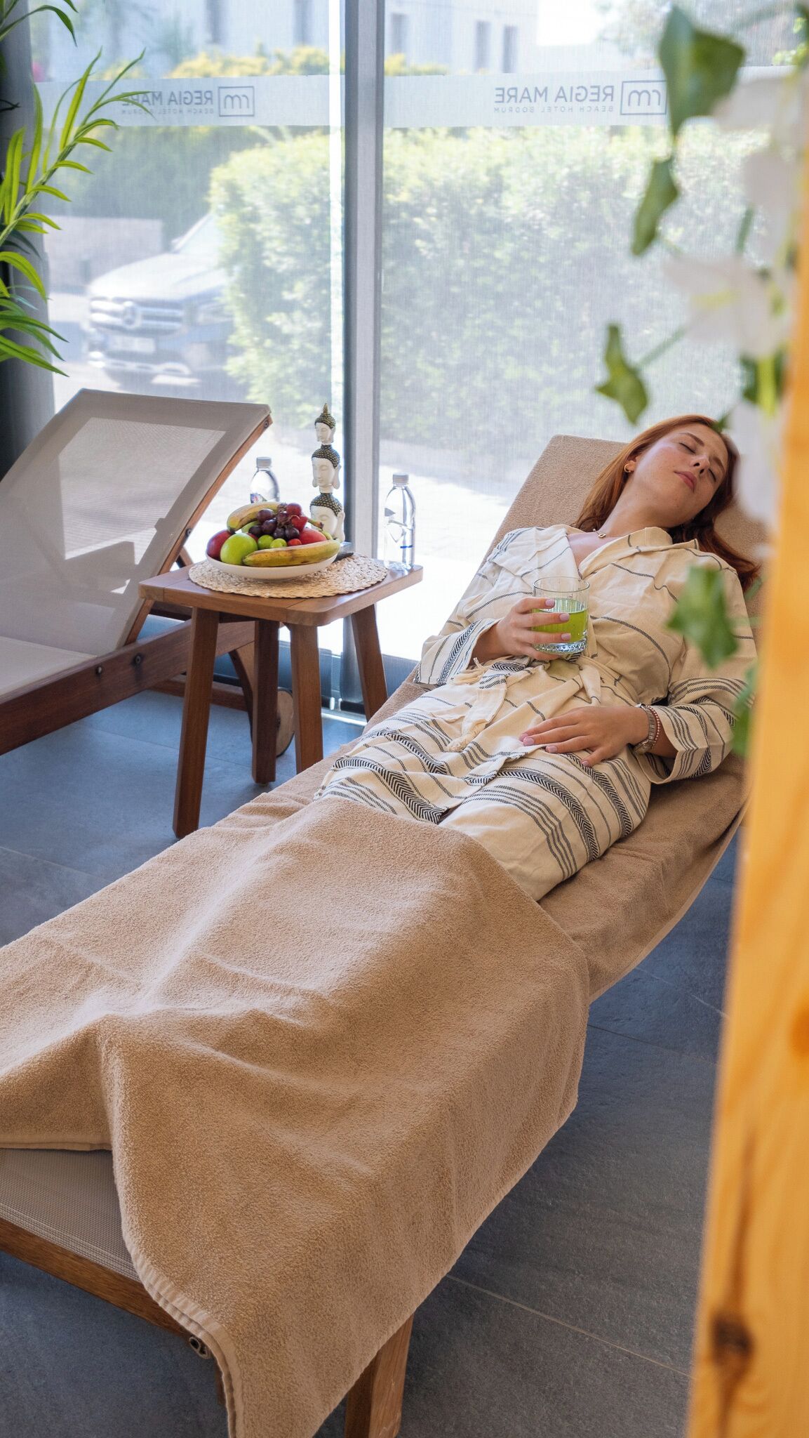 Eine Person liegt auf einer Massageliege in einem Raum mit Blick auf eine grüne Landschaft.