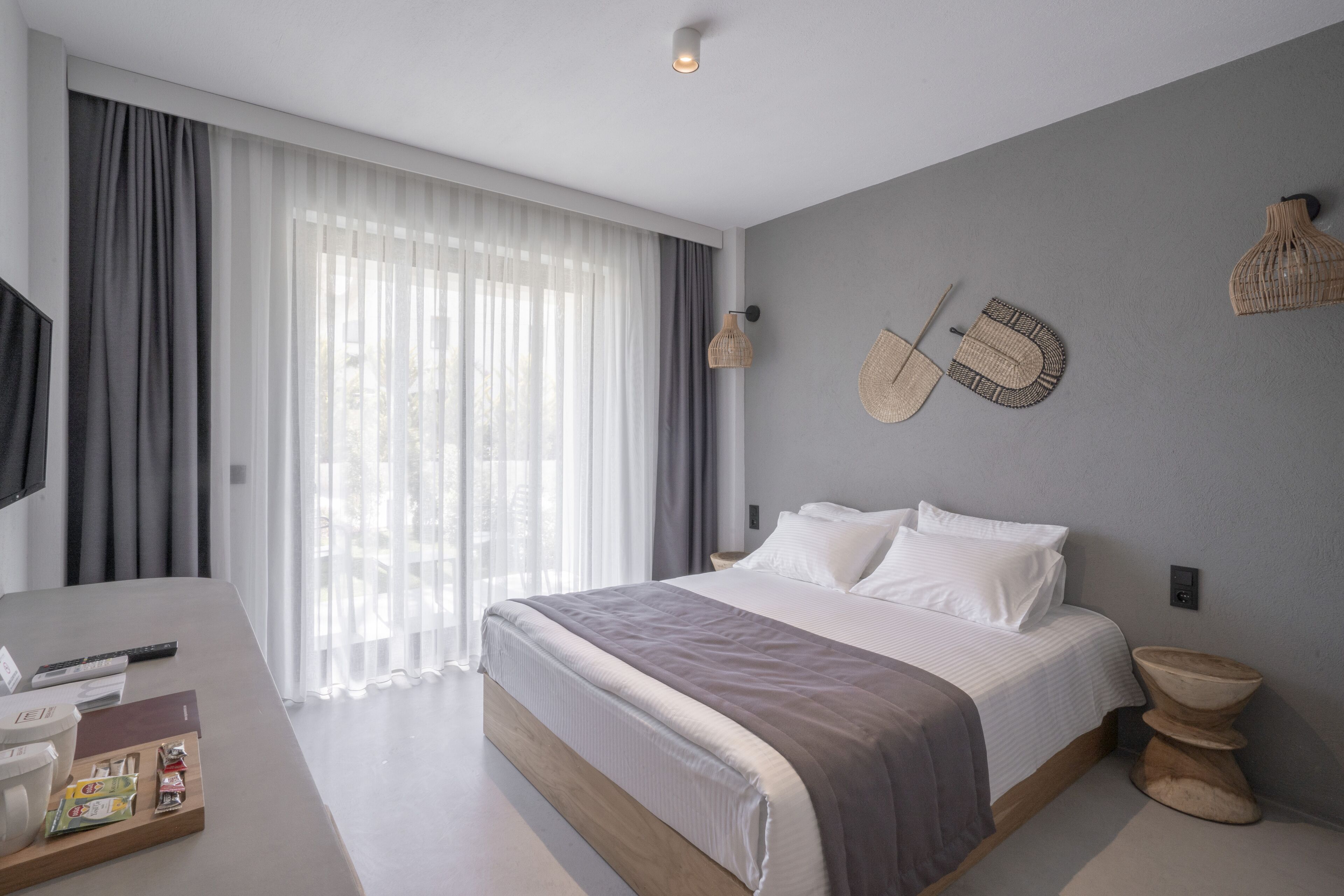 Een moderne slaapkamer met een groot bed, een nachtkastje, een televisie en een raam met gordijnen.
