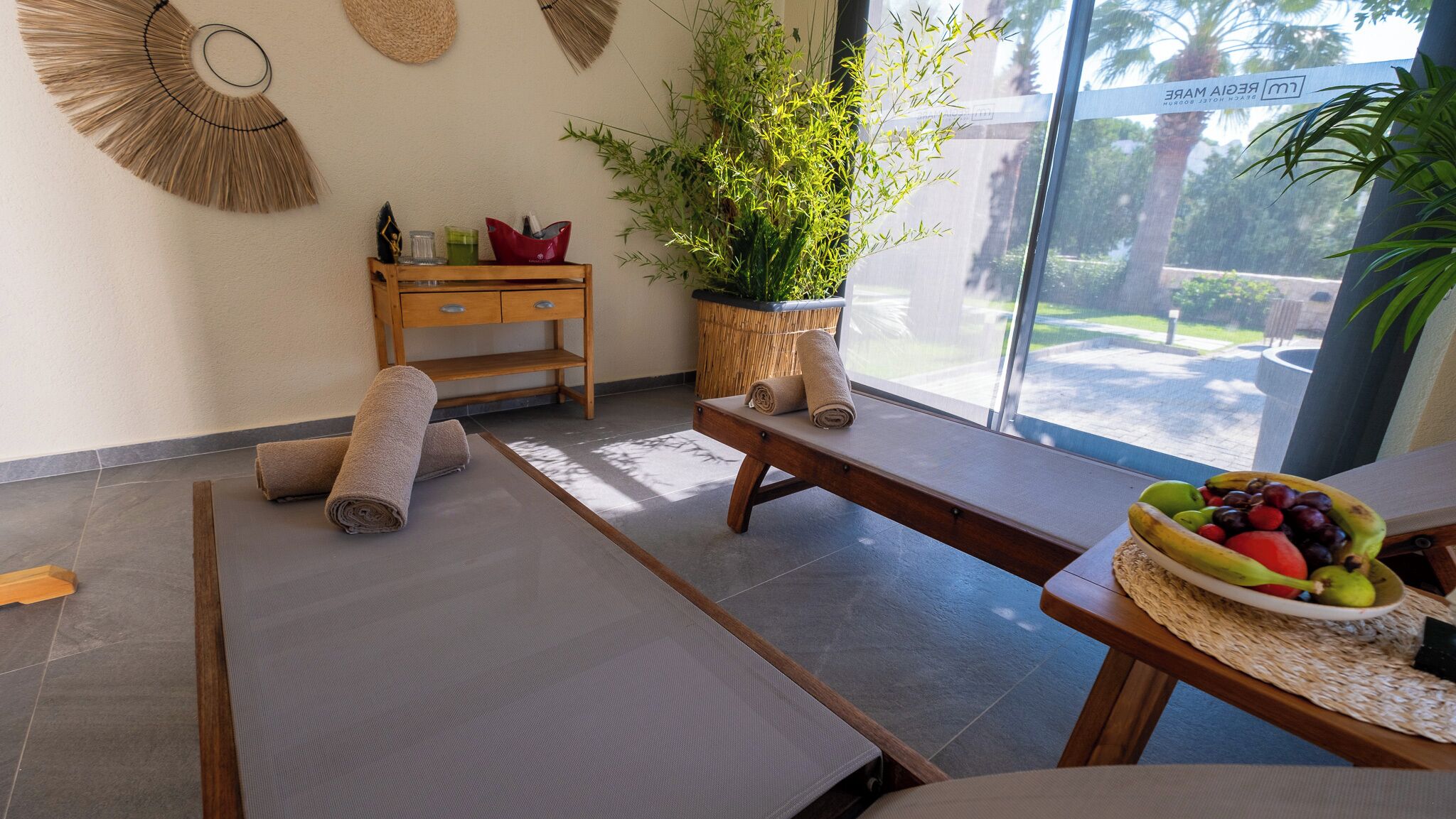A spa room with a massage table, a wooden bench, a potted plant, and a fruit bowl.