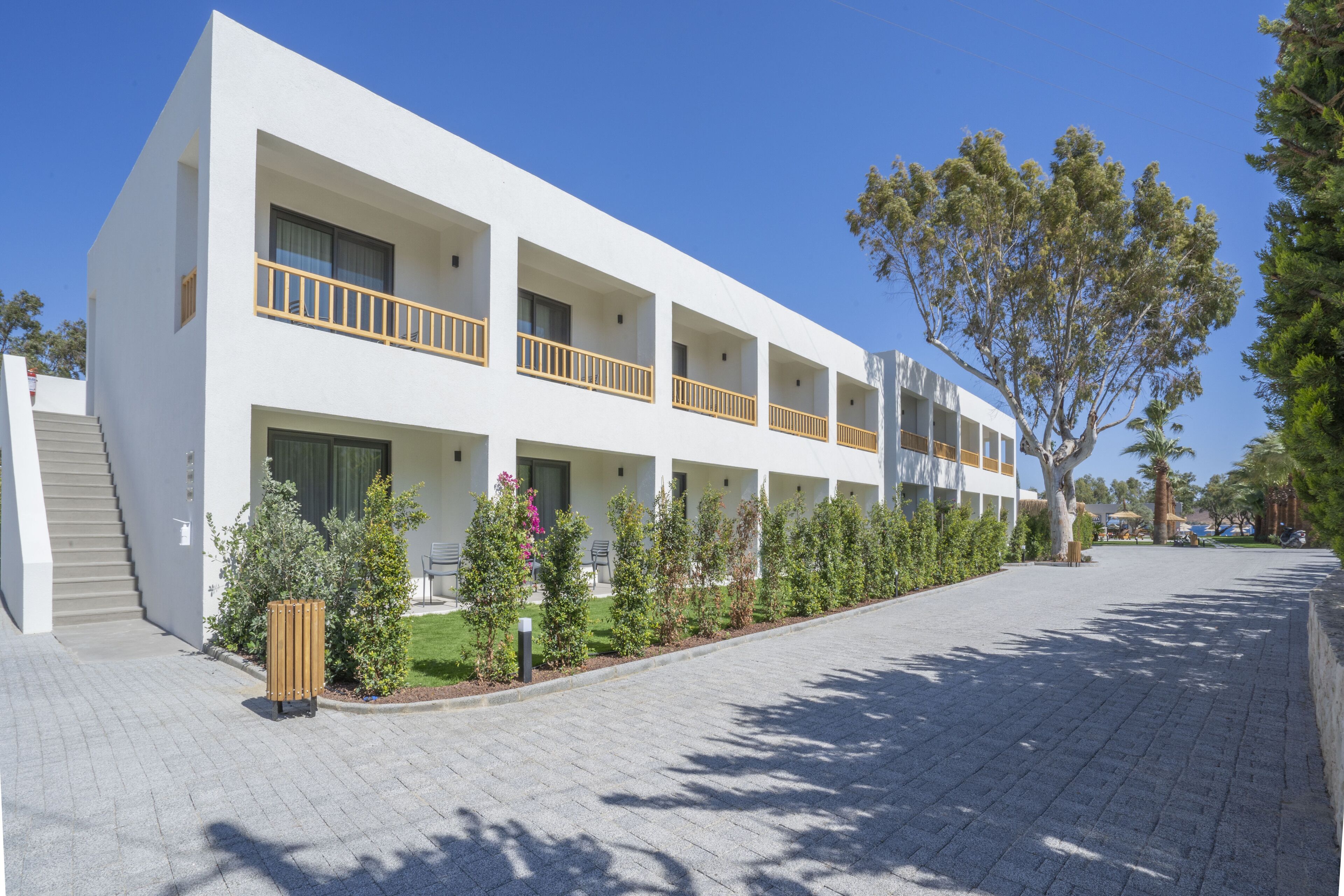 Ein modernes, mehrgeschossiges Hotel mit weißer Fassade, Balkonen und einem gepflasterten Zugangsweg.