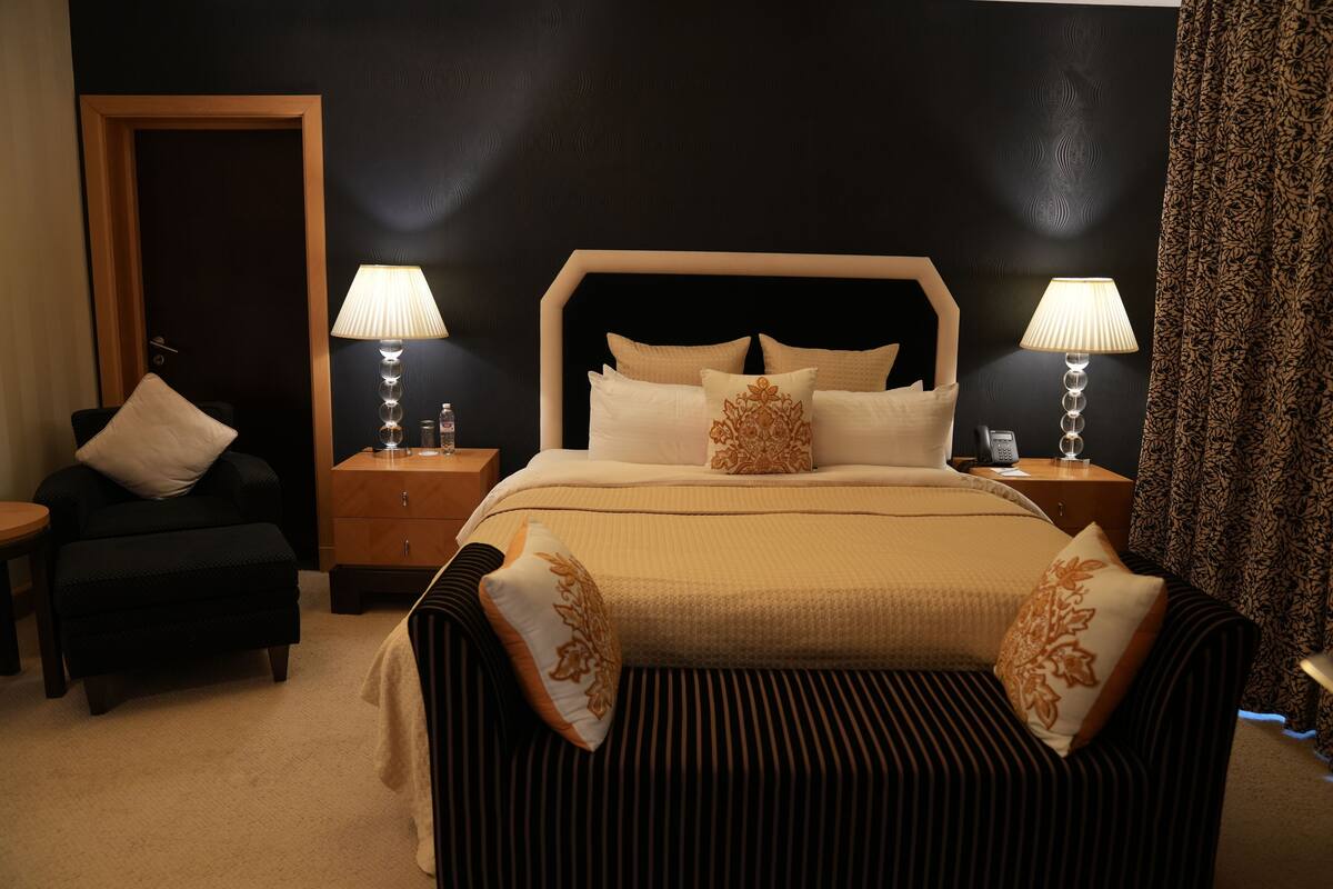 Una habitación de hotel con una cama grande, dos mesitas de noche con lámparas, una silla y un armario.