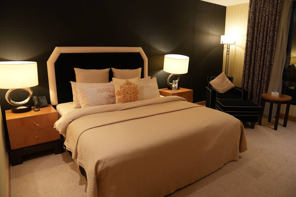 Una cama bien hecha con cabecera, dos mesitas de noche con lámparas, una silla pequeña y un tocador con un teléfono.