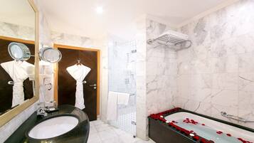 A bathroom with two sinks, a large mirror, a shower, and a bathtub with rose petals.