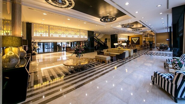 Eine geräumige Lobby mit einer zentralen Sitzecke, einer Treppe und einer Rezeption.