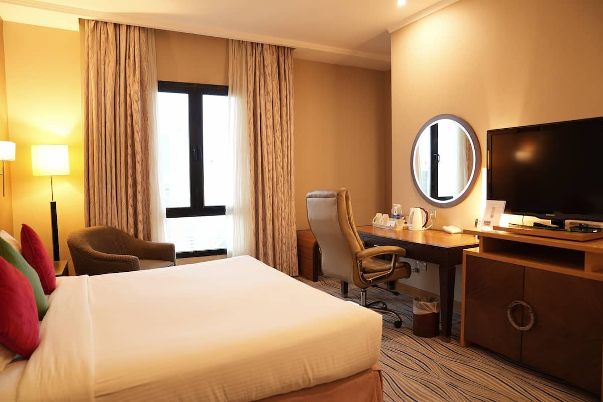 Una habitación de hotel con una cama grande, un escritorio con silla, televisión y ventana con cortinas.