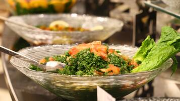 Un bufé con diversos platos, incluyendo una ensalada de hojas verdes y tomates.