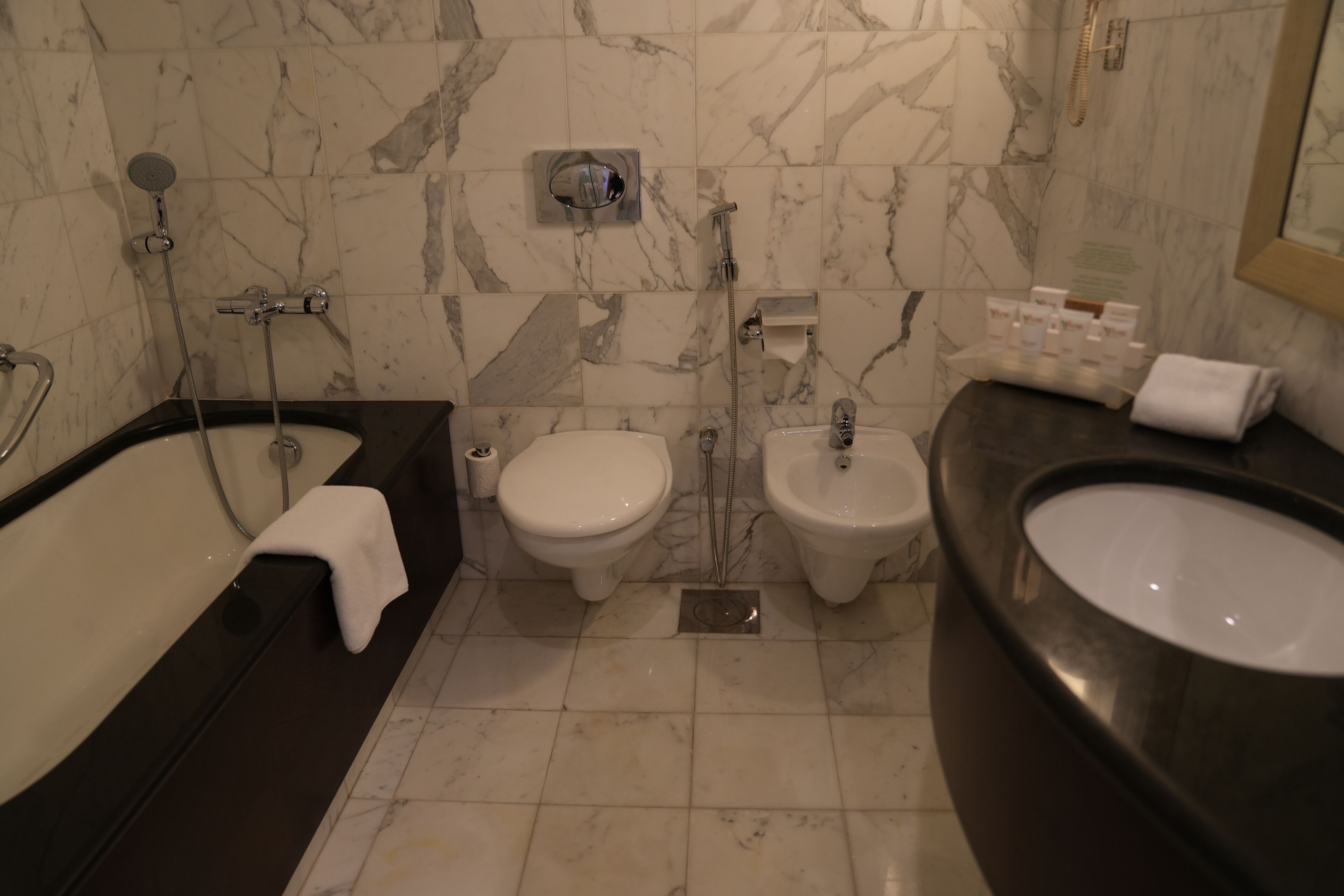 Un baño con bañera, dos inodoros y un bidé.